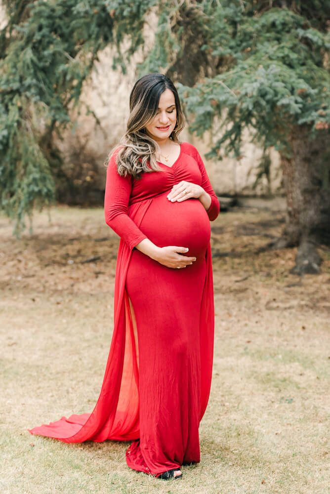 Photograph of an Edmonton maternity photography session of an expecting mother wearing a red dress with a train from Cynthia Priest Photography's client closet to demonstrate maternity clothing in Edmonton
