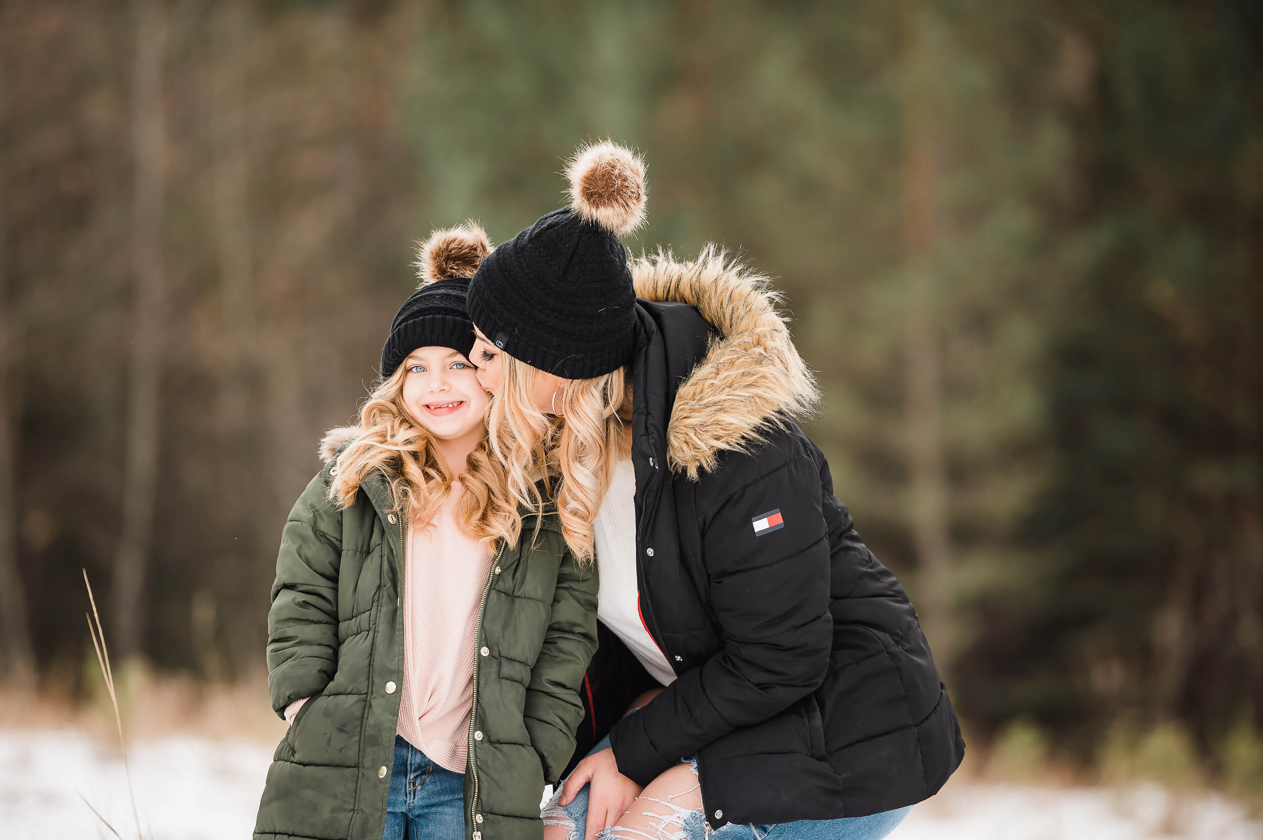 A mom kissing her daughter during a family winter session while playing outdoors in Edmonton