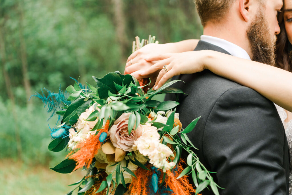 Close up of bride's bouquet and wedding ring while her husband nuzzles into her embrace
