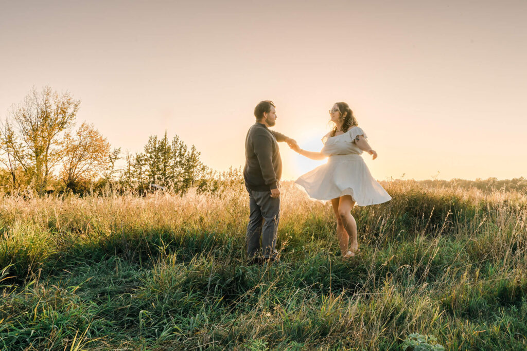 An Edmonton couple having fun at a golden hour session with Cynthia Priest Photography - female is wearing solid white dress while her partner is wearing a green sweater and grey pants