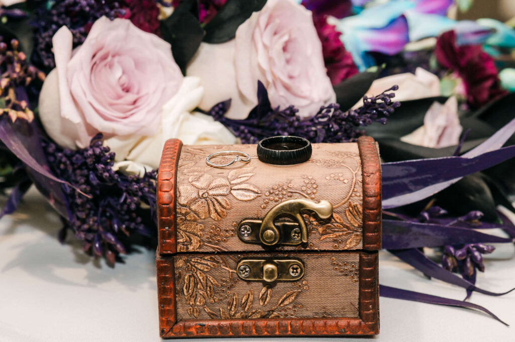 Close Up detail of Wedding Rings on a wooden box with flowers in the background