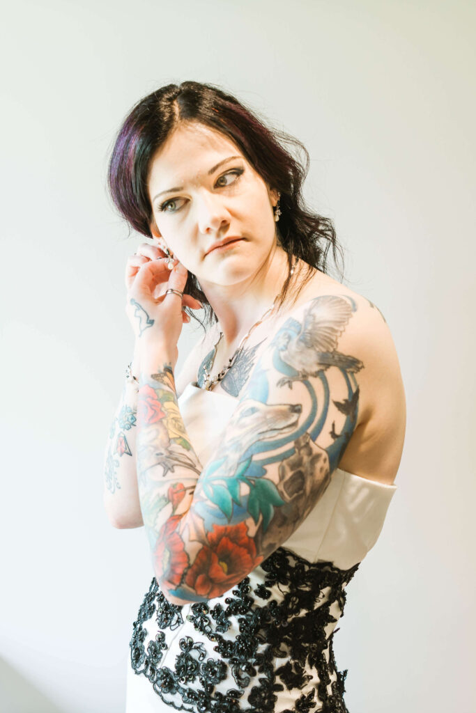 a woman with tattoos on her arms adjusting her earrings in a wedding dress