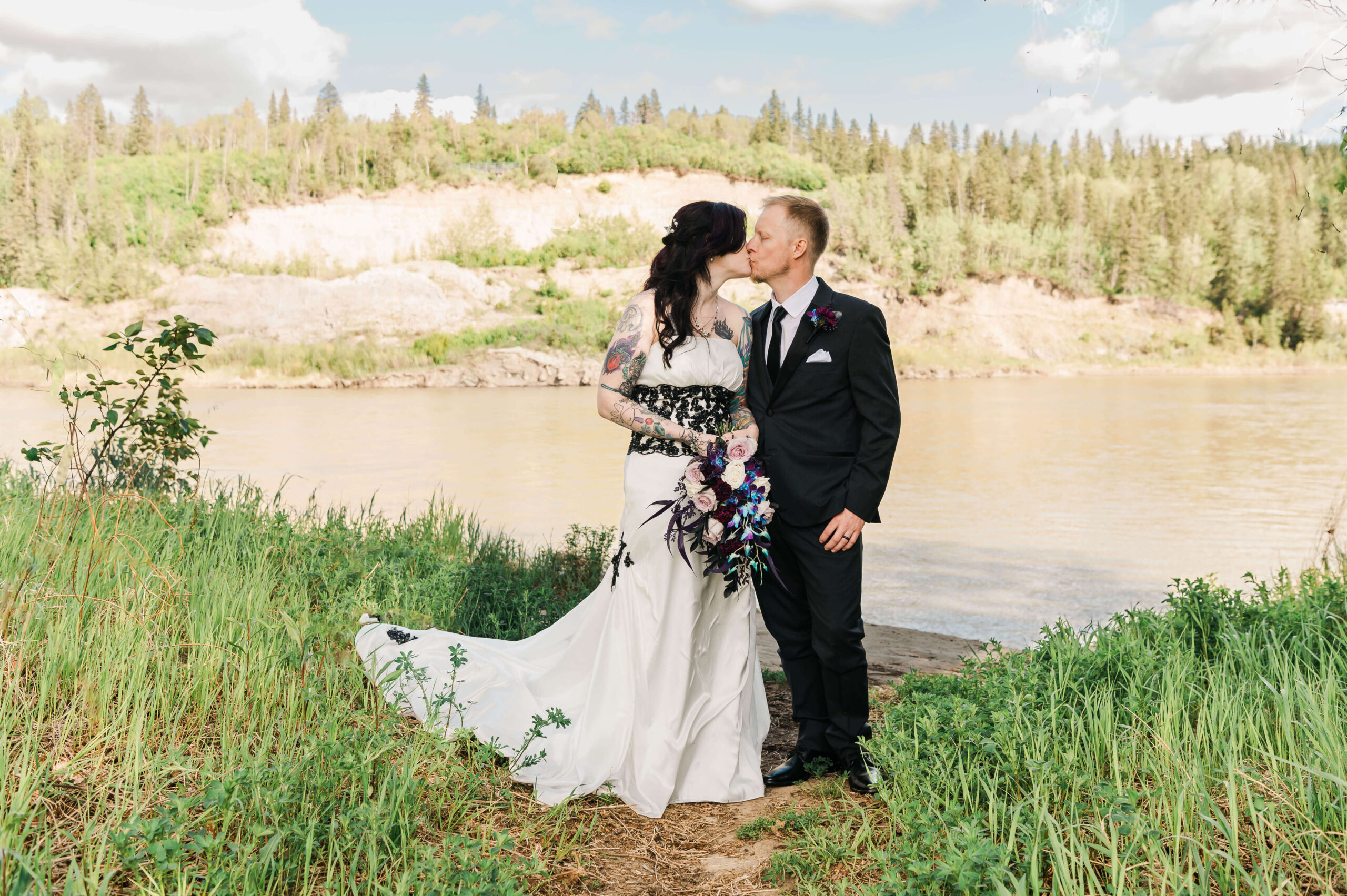 a man in suit and woman in wedding dress kissing in front of the North Saskatchewan river in Edmonton for a Yorath House Wedding