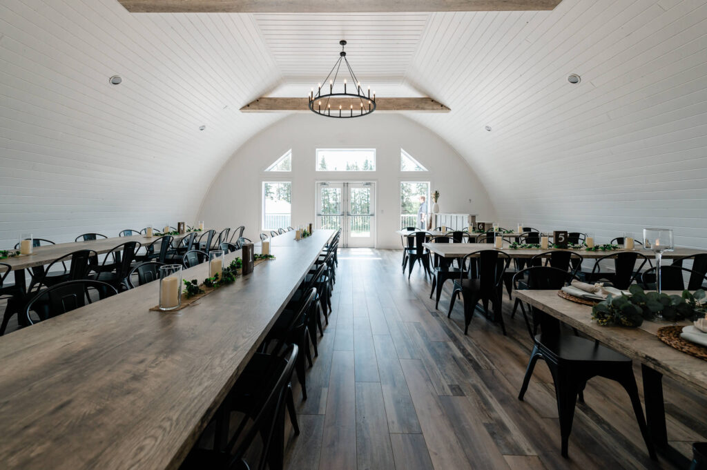 A modern white interior of a barn with high ceilings with long tables set up for a wedding reception at Beyond the Meridian