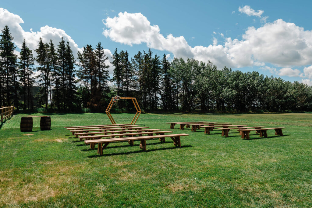 Outdoor ceremony area shaded by trees with a hexagonal arch and wooden benches