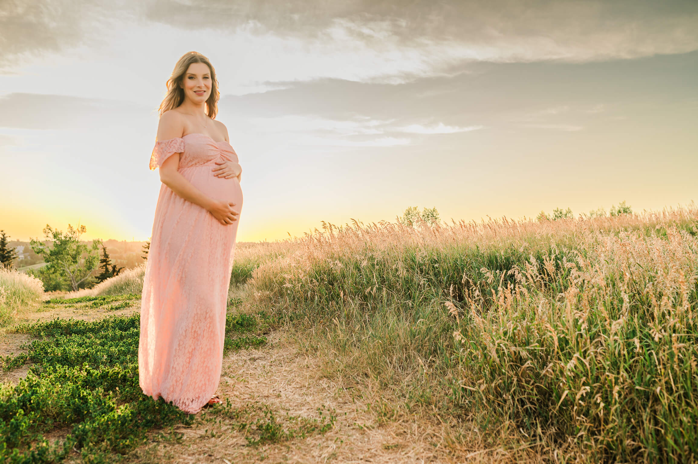 A pregnant mom in a baby pink maternity dress holding her bump to feature a blog article on Edmonton midwives