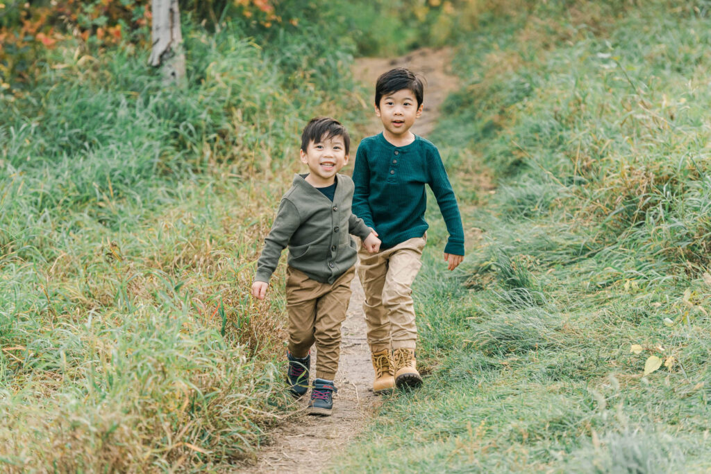 Two young Edmonton children in green tops and khaki bottoms running towards the camera, having a lot of fun with Cynthia Priest Photography