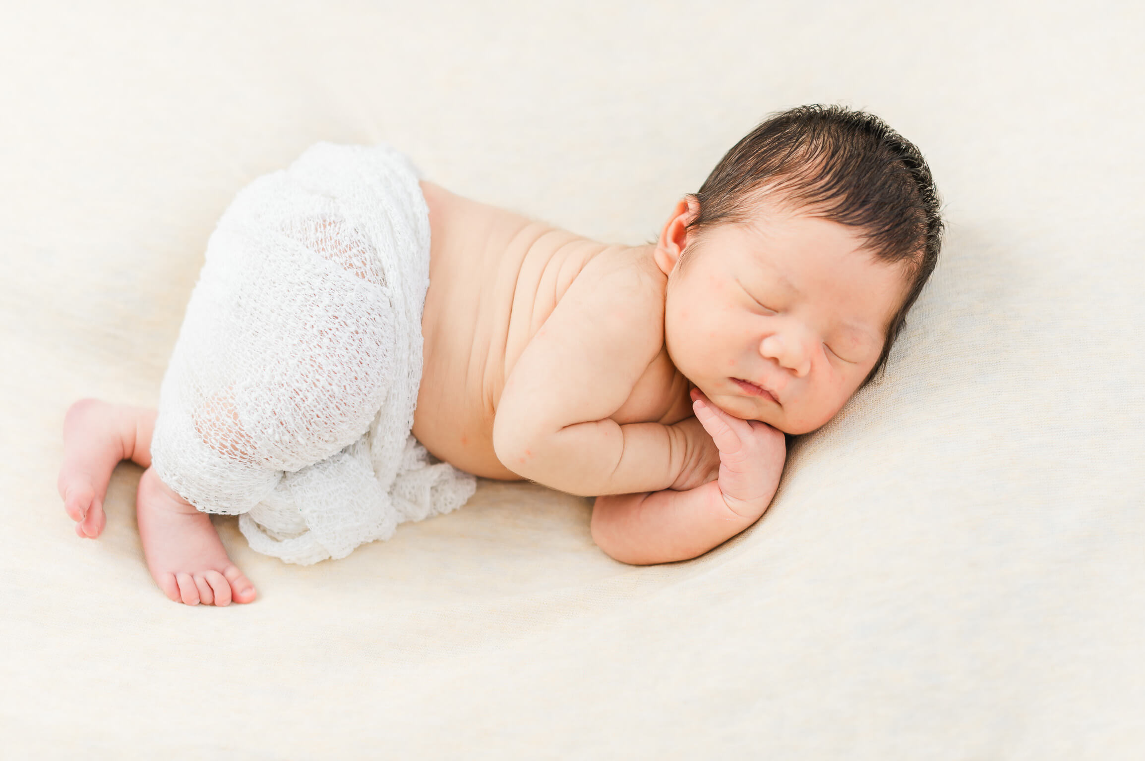 A baby boy sleeping soundly in a white swaddling blanket as he is wearing a diaper from an Edmonton diaper service