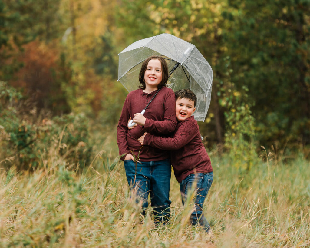 Two brothers wearing burgundy long sleeved shirts and blue denim having fun in the rain