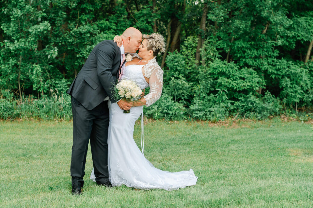 a man in a wedding suit and woman in a wedding dress kissing in a field