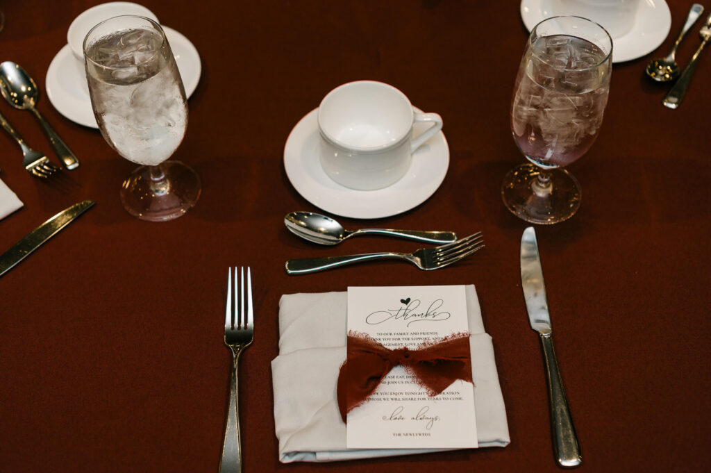 a red table cloth with silverware and a napkin with a bow on it along with a Thank You card for wedding guests