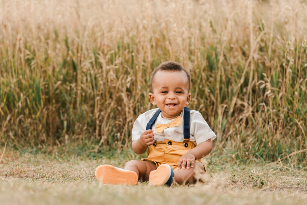 Smiling adorable 7 month old baby in a field wearing a bow tie and suspenders