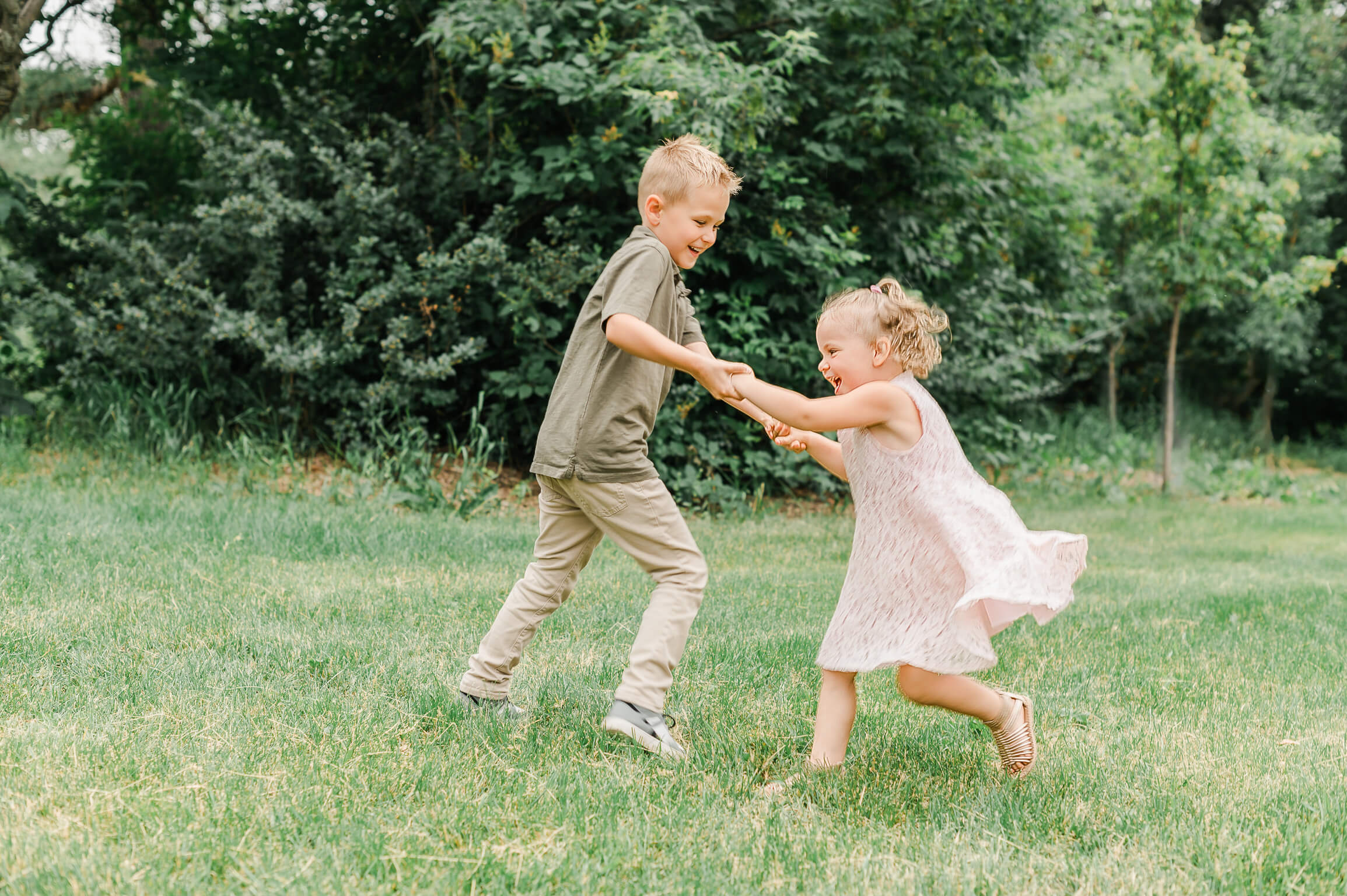 a boy and girl holding hands and dancing in grass to feature an article about imaginative play at Mastermind Toys Edmonton