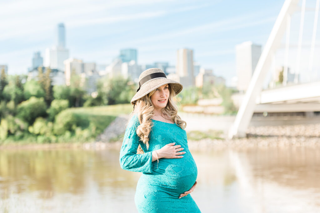 A mom wearing a teal dress from Cynthia Priest Photography's client closet at an outdoor maternity photo session by Walterdale bridge