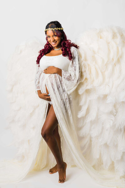 Expectant mom wearing a white dress and angel wings with a goddess crown