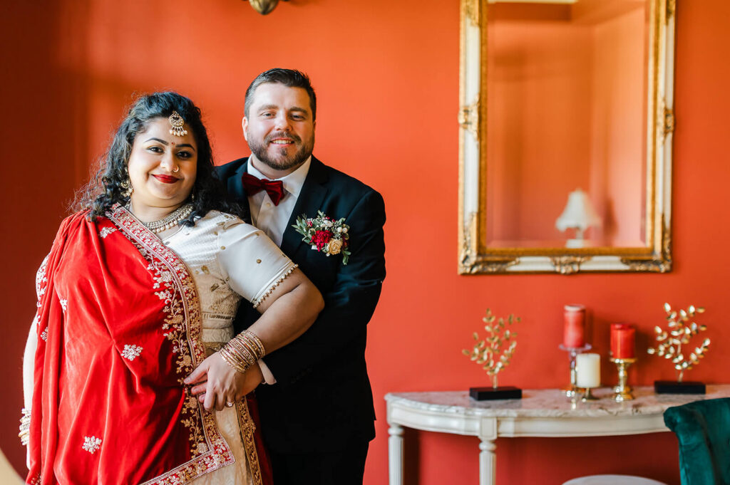 Luxury mansion esthetic matching the deep red sari of the South Asian bride while the white groom embraces his bride