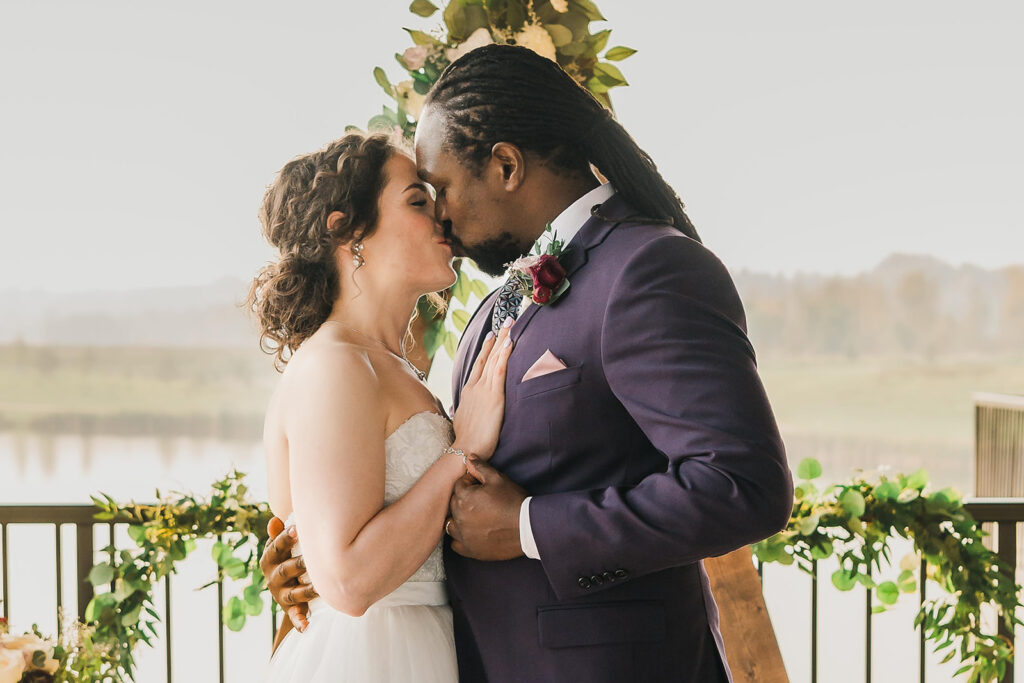 A kiss of a wedding couple at an outdoor ceremony with the lake in the background