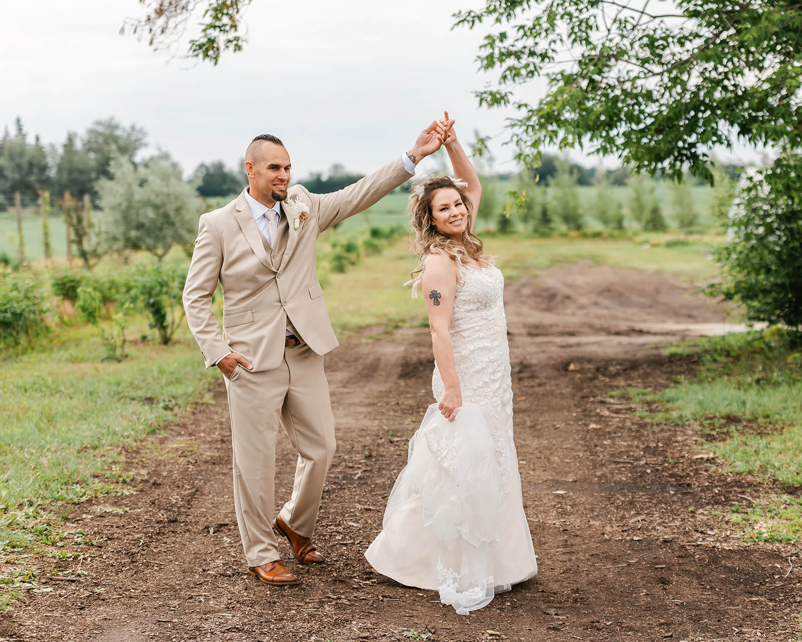 Groom spinning bride on a garden path surrounded by lush green orchard rows