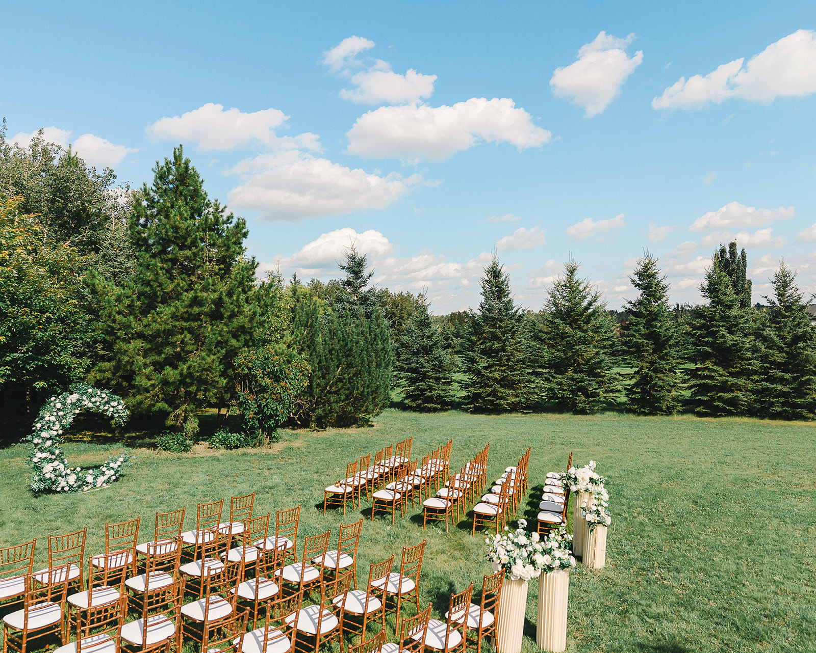 Drone view of the outdoor ceremony setup with Chiavari chairs and a floral arch at a Dragonfly Inn Sherwood Park wedding