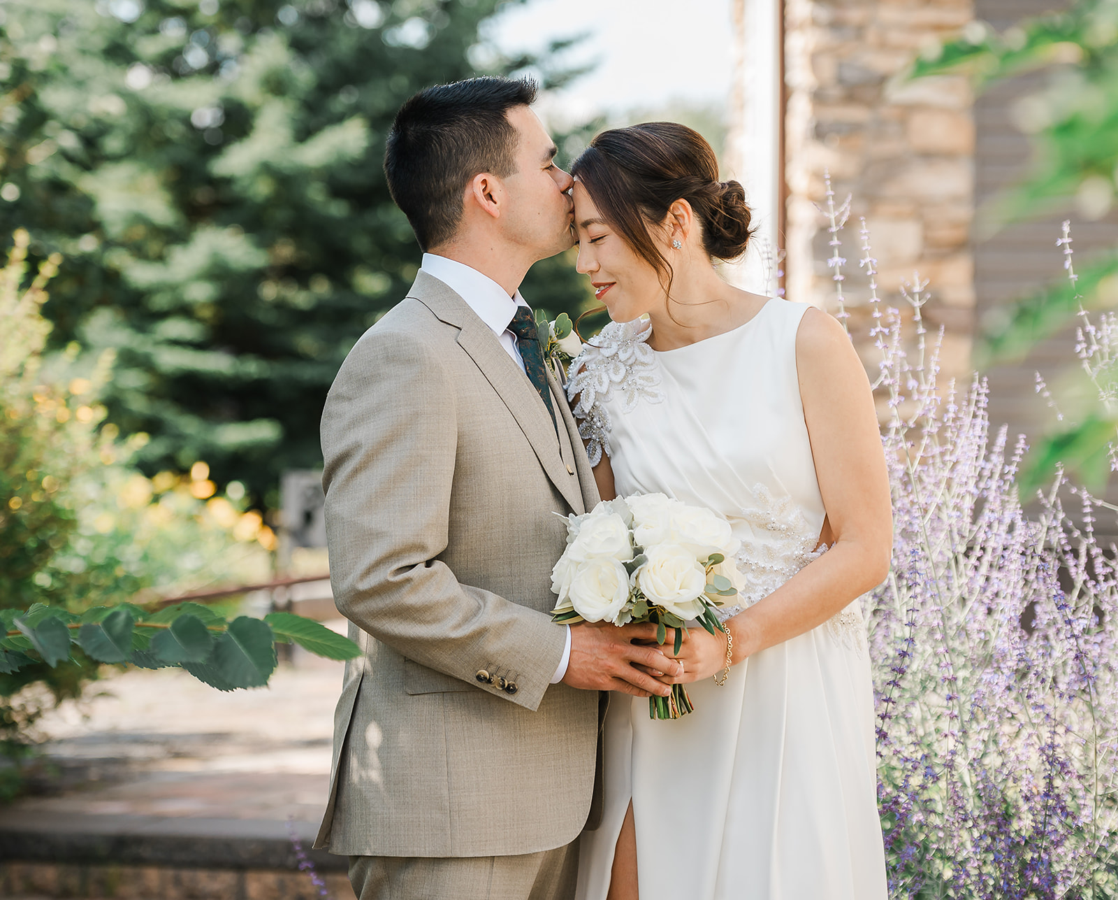 Groom kisses bride on the forehead beside lavender at their Dragonfly Inn Sherwood Park wedding